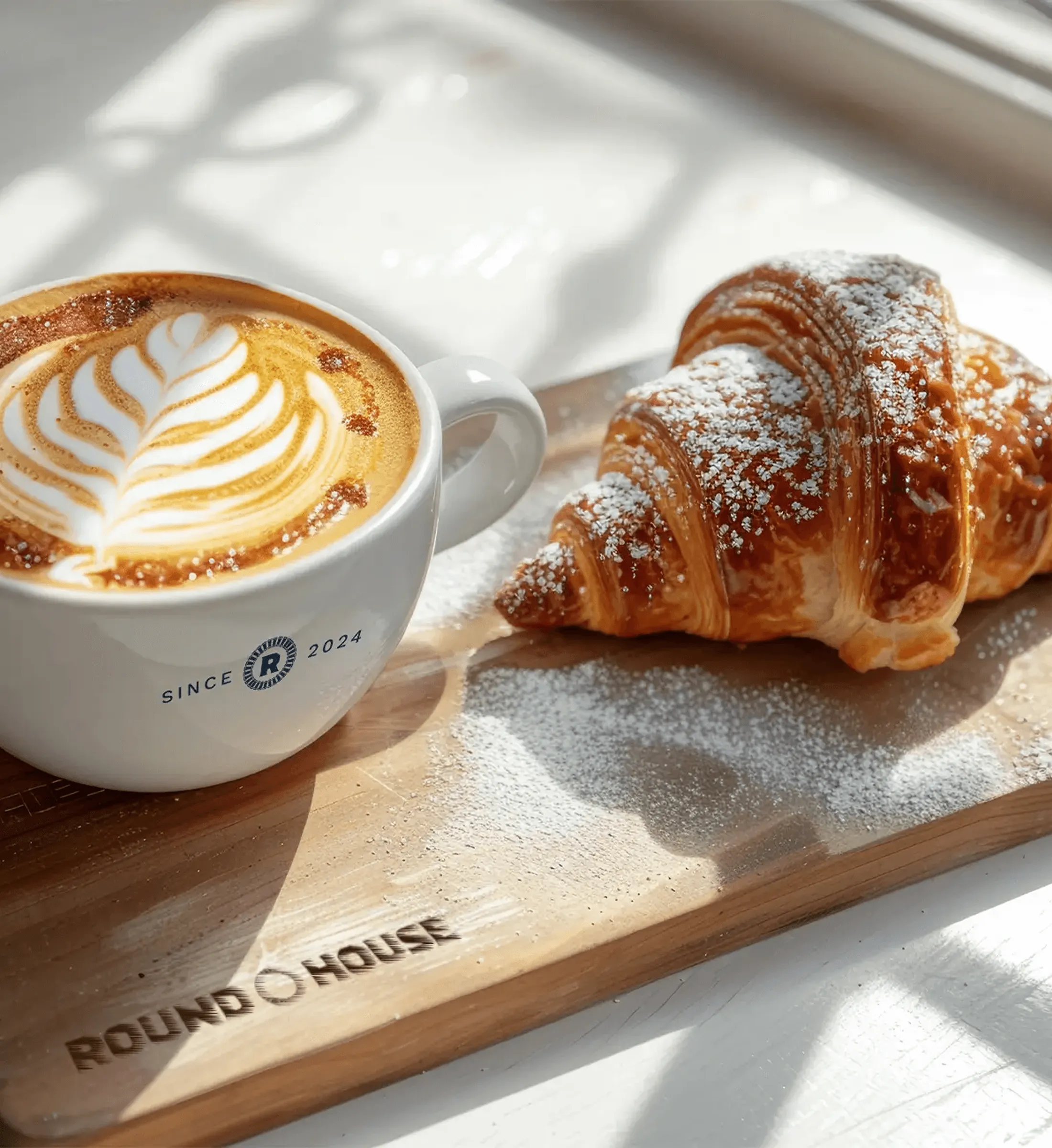 Latte and croissant on a Roundhouse-branded serving board